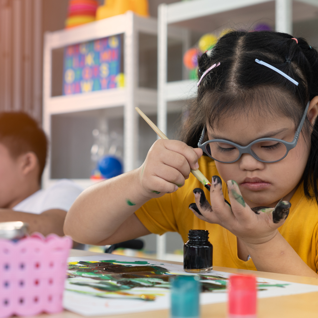 A young girl with Down Syndrome paining a picture on paper in an educational setting