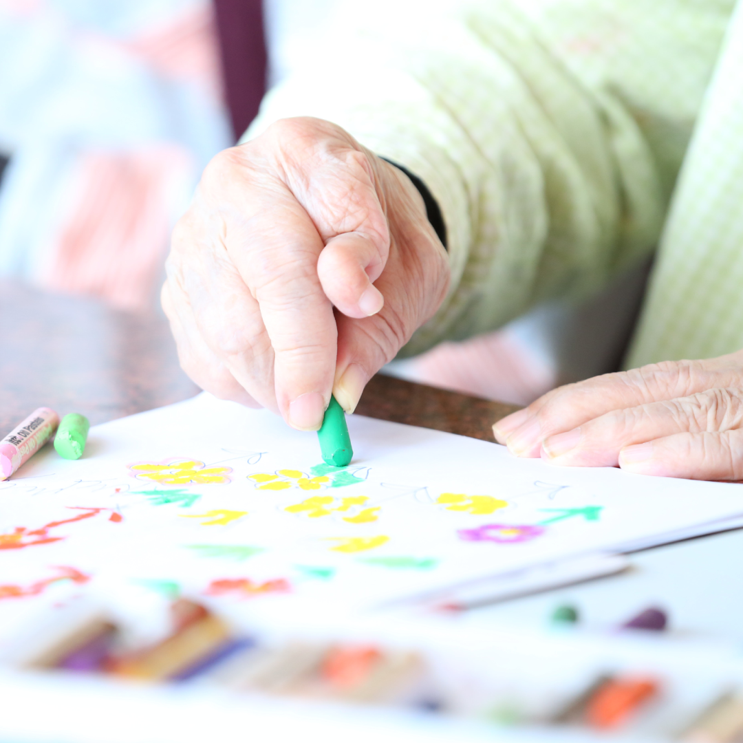 an elderly hand colouring a drawing on a sheet of paper