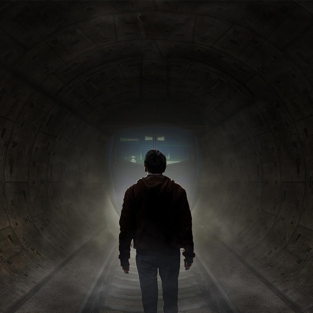 Shot from behind of a man walking down a dark, foreboding tunnel. The picture is in mono tone