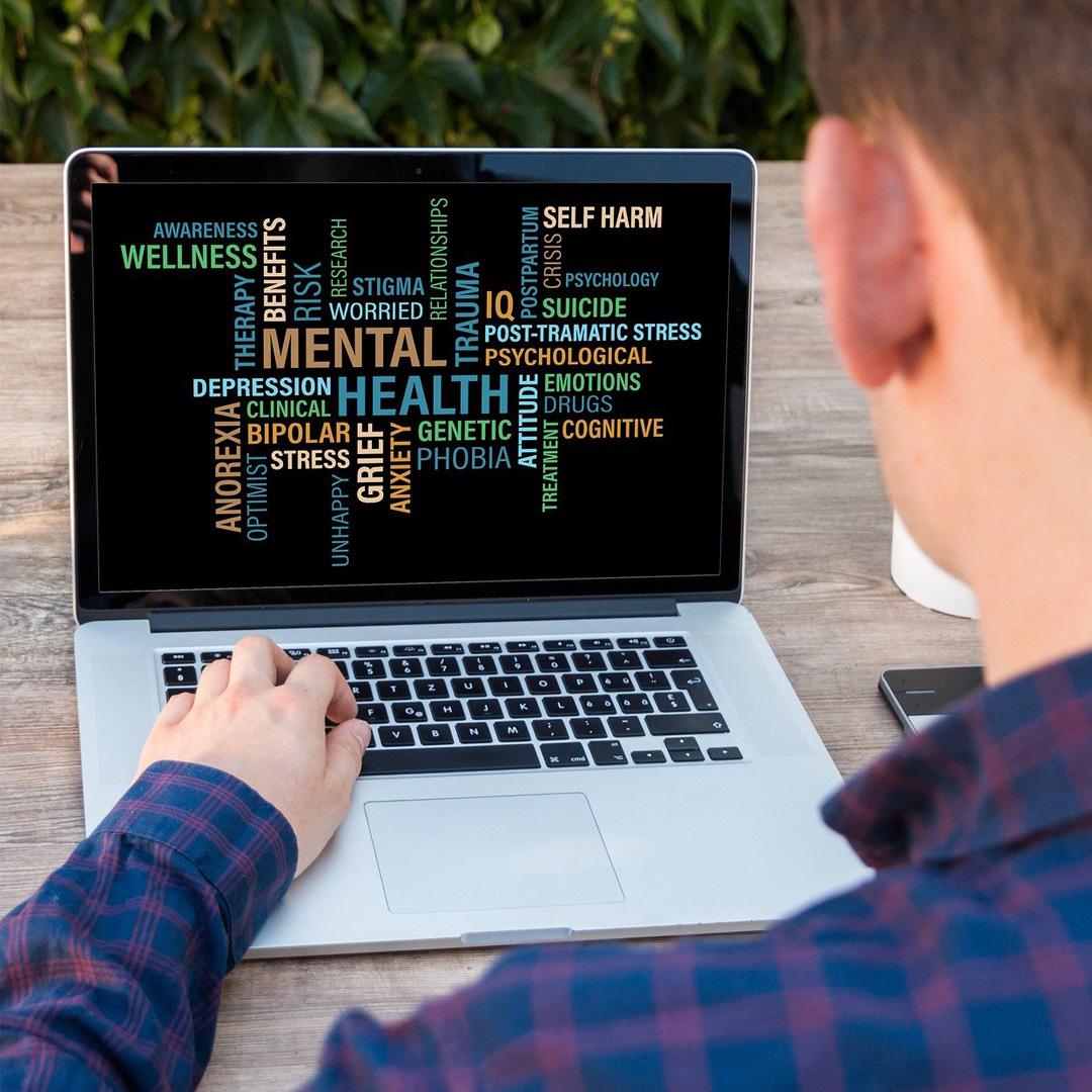 Male child sitting at a laptop in front of a screen showing words related to mental health, such as wellness and stress.