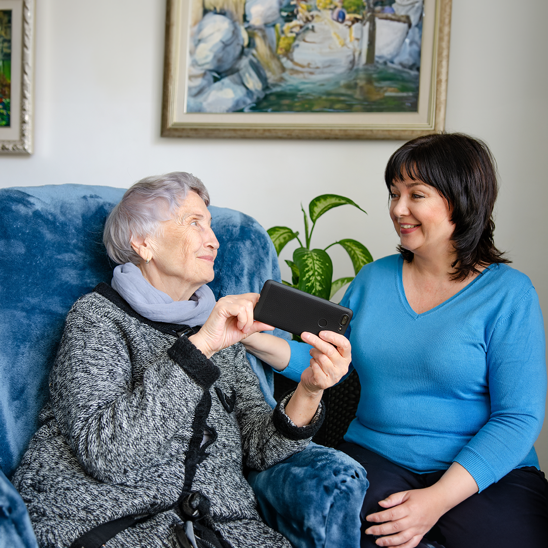 An elderly lady looking at a lady in a blue top. Both are smiling at each other