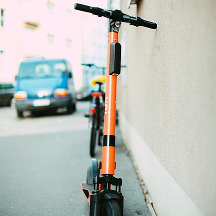 An orange electronic scooter resting up against a wall