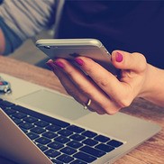 Person looking at a mobile phone in front of a laptop