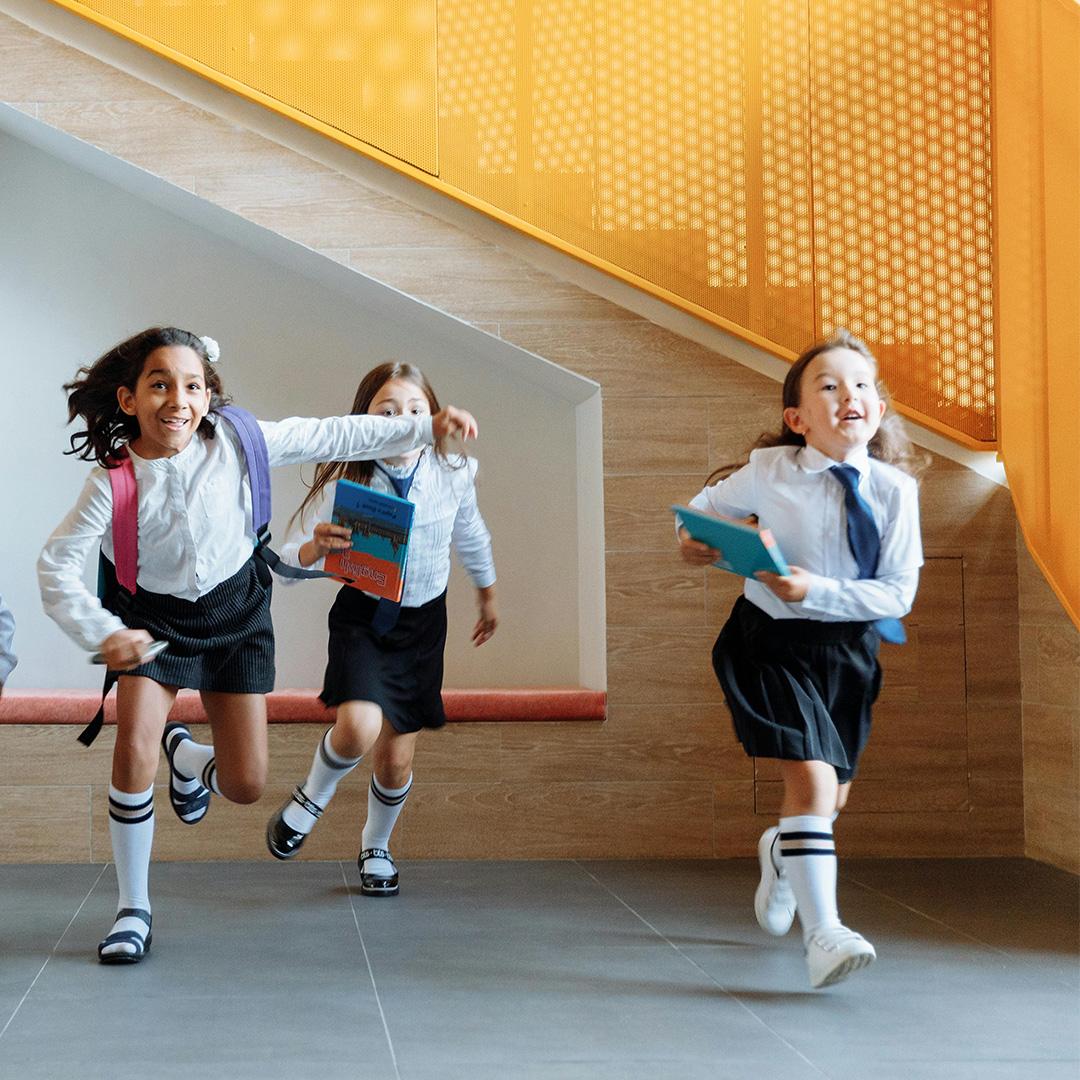 Three primary school girls smiling and running whilst wearing uniform