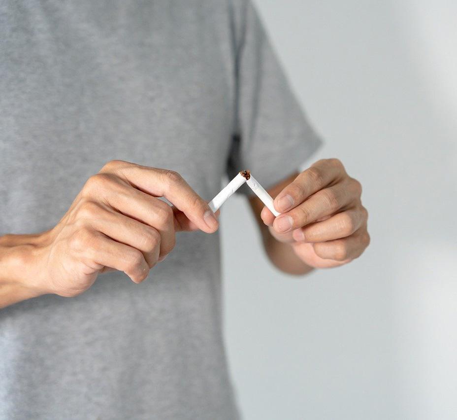 A man wearing a grey t-shirt snaps a cigarette in half. The mid section of the man can be seen but not his head or legs.