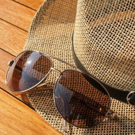 A sun hat and aviator sunglasses placed on a wooden table